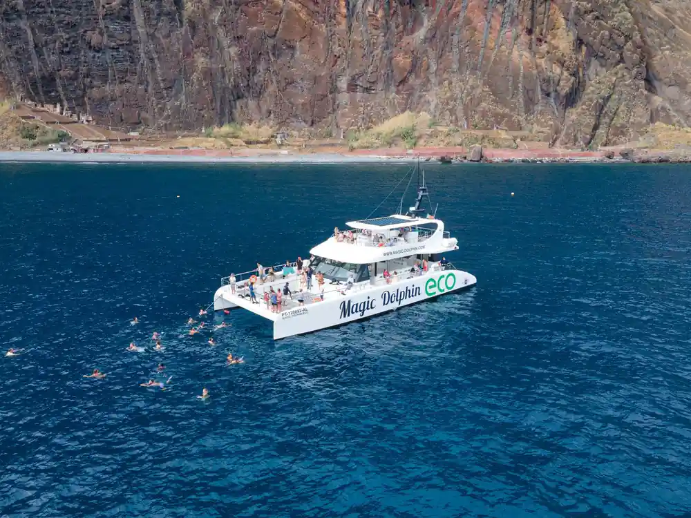 The catamaran at anchor below a red headland