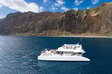 The Magic Dolphin Eco catamaran full of guests below a red cliff