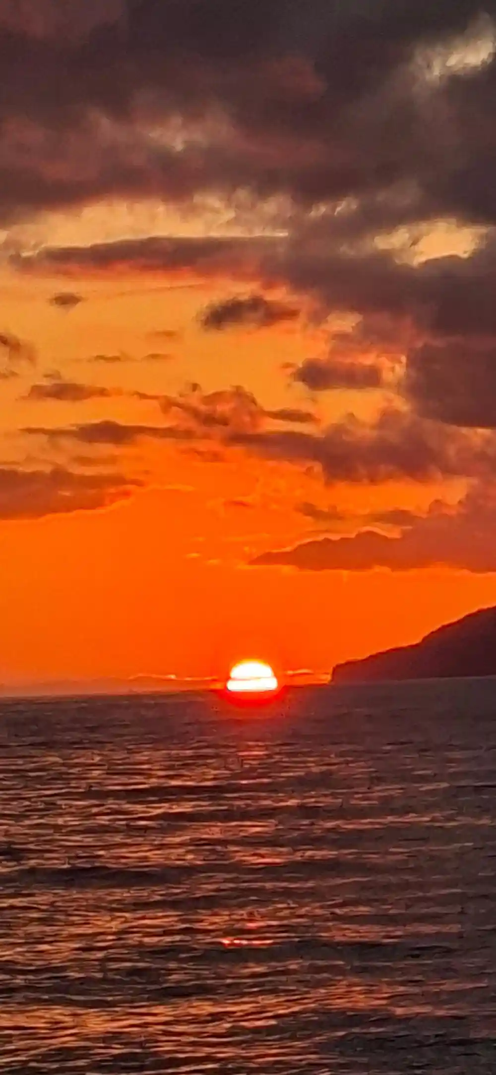 A red sunset over the sea behind a headland