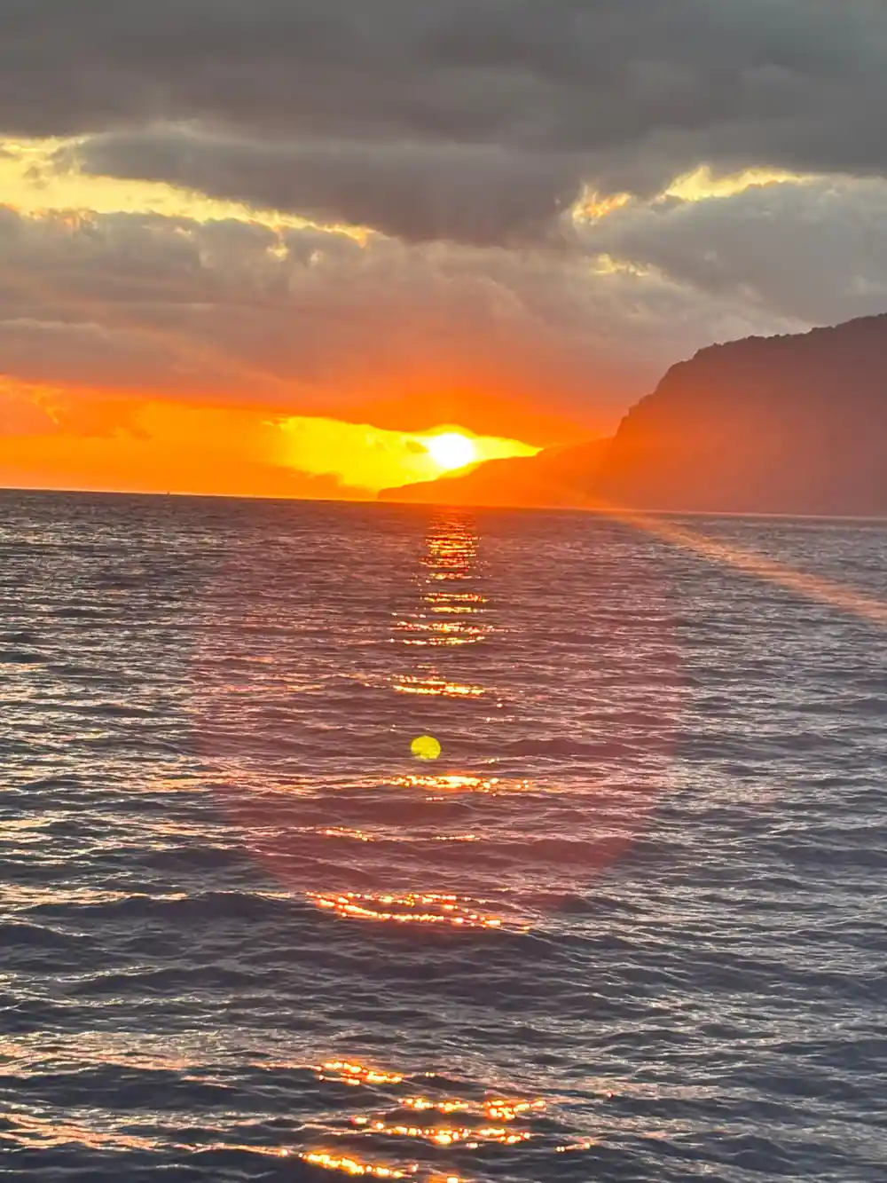 The sun setting on the water beside a cliff