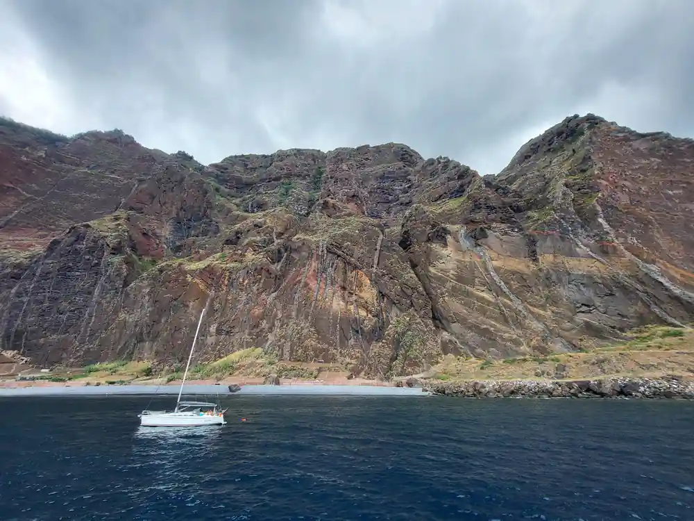 A yacht anchored below a rugged red headland
